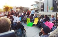 Angekettete Menschen im Rollstuhl mit Protestplakaten
