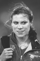 Foto: Schnappschuss- junge Frau, aus der Stirn gekämmtes, zu Zopf geflochtenes, etwas zerzaust Haar. Offizielle Paralympics-Sportjacke, eine Hand hält breiten Träger einer Tasche auf der Schulter. Blick aus dem Augenwinkel nach rechts, leicht lächelnd.