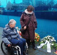 Sigrid Arnade (mit Rollstuhl) und Martina Puschke blicken auf den Kranz des Deutschen Behindertenrates an der Blauen Wand des T4-Gedenkortes