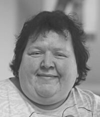 Portraitfoto, Petra Groß grinst in die Kamera. Sie hat einen breiten Kopf, kurze dunkle lockige Haare, markante Nasenflügel, schmale Augen und ein ausgeprägtes Doppelkinn.