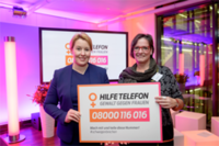 Bundesministerin Dr. Franziska Giffey und Martina Puschke halten das Schild: Hilfetelefon Gewalt gegen Frauen hoch. (