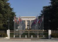 Foto: Seiteneingang des Palais des Nations in Genf, dem europäischen Hauptsitz der Vereinten Nationen. Auf dem hohen Steinsims des Eingangs steht „United Nations - Nations Unies und dazwischen das Logo der Vereinten Nationen.